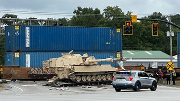 Military mobile artillery vehicle being hauled on a semi-truck collides with train.