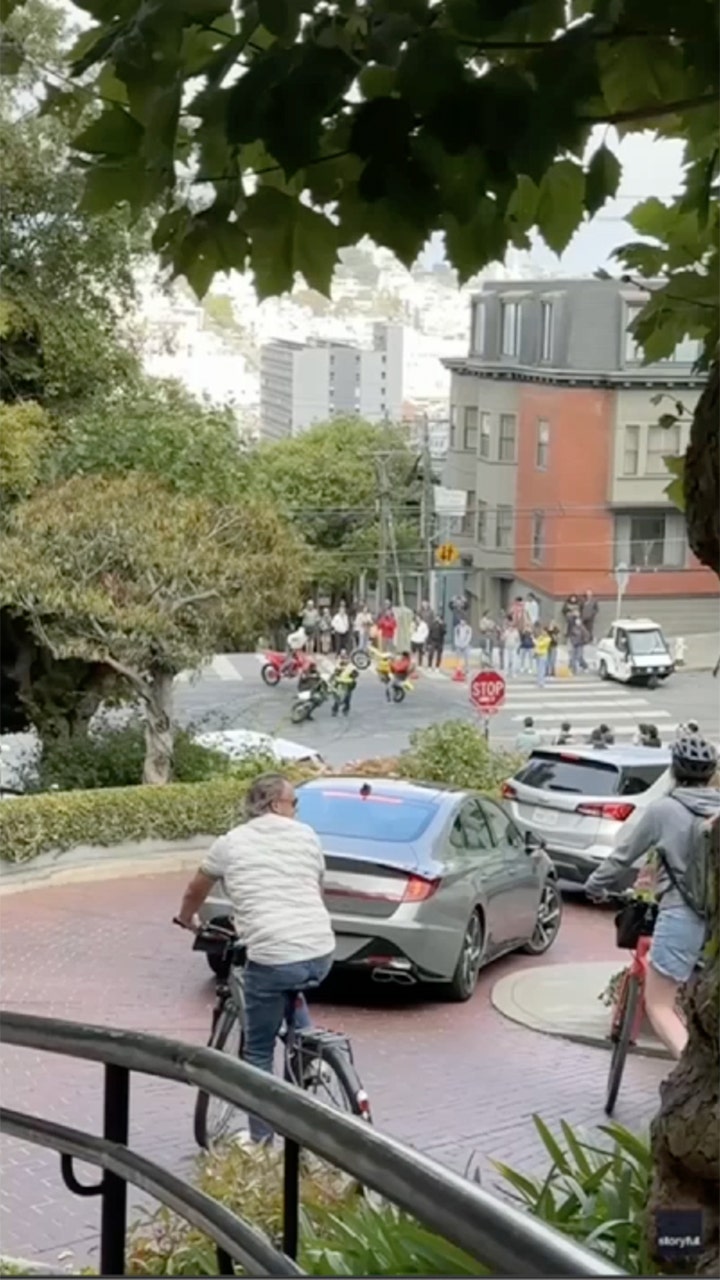 Masked motorcyclists surround San Francisco traffic officer in tourist district.